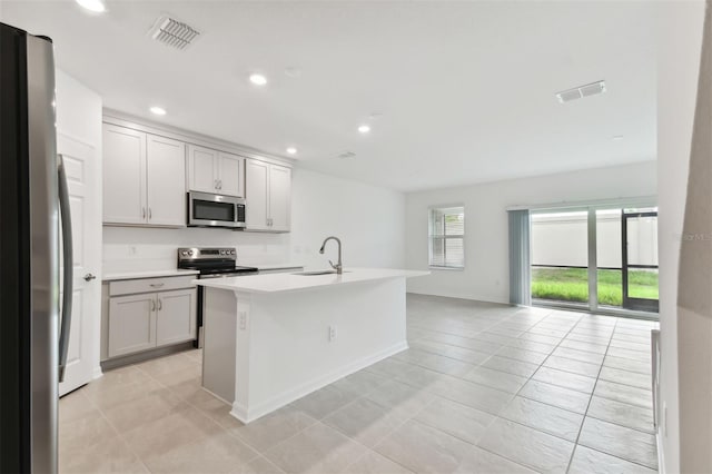 kitchen with a center island with sink, gray cabinets, stainless steel appliances, light tile patterned flooring, and sink