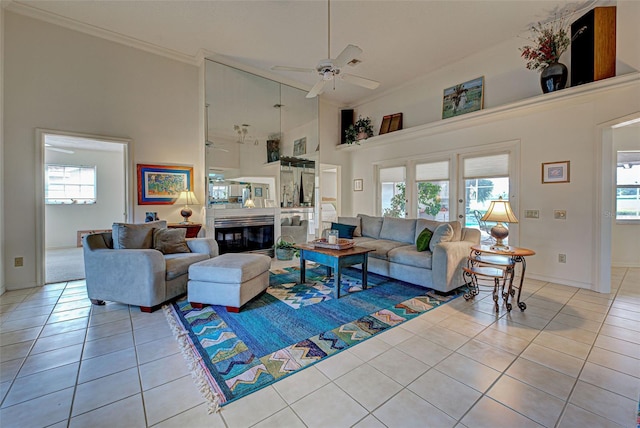 tiled living room with ceiling fan, crown molding, a towering ceiling, and a healthy amount of sunlight