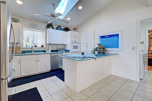 kitchen featuring sink, stainless steel appliances, white cabinets, vaulted ceiling with skylight, and light tile patterned flooring