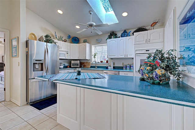 kitchen featuring lofted ceiling with skylight, light tile patterned floors, a textured ceiling, appliances with stainless steel finishes, and white cabinetry