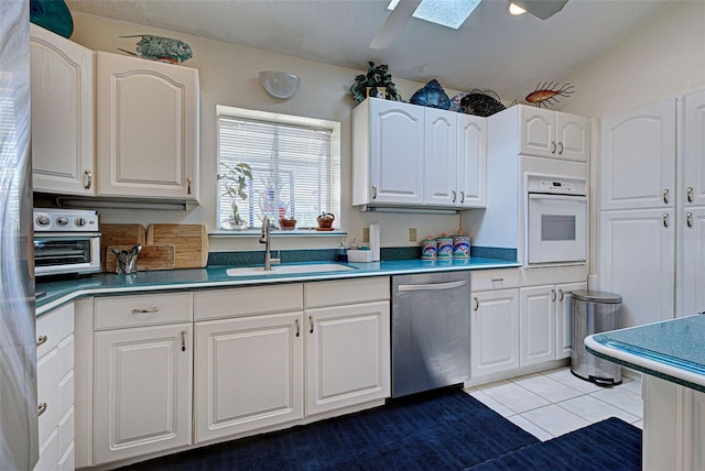 kitchen featuring stainless steel dishwasher, sink, light tile patterned floors, white cabinets, and oven