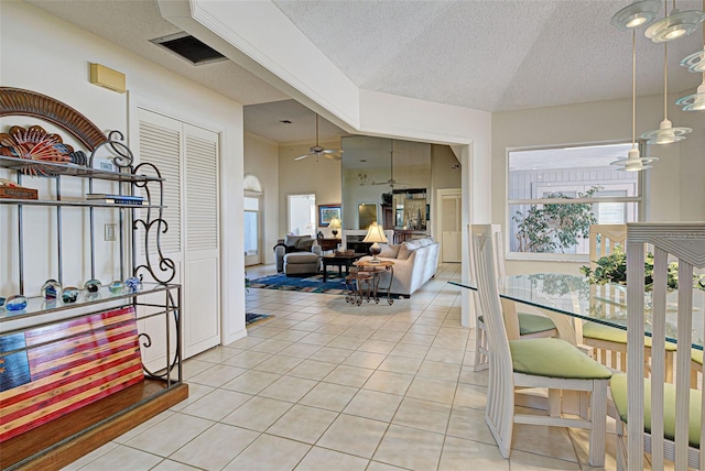 dining area with ceiling fan, light tile patterned flooring, a textured ceiling, and vaulted ceiling