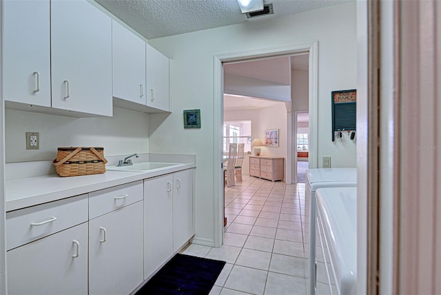 laundry area with cabinets, a textured ceiling, sink, light tile patterned floors, and separate washer and dryer