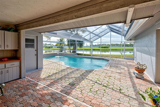 view of pool with a lanai, a patio area, and a water view