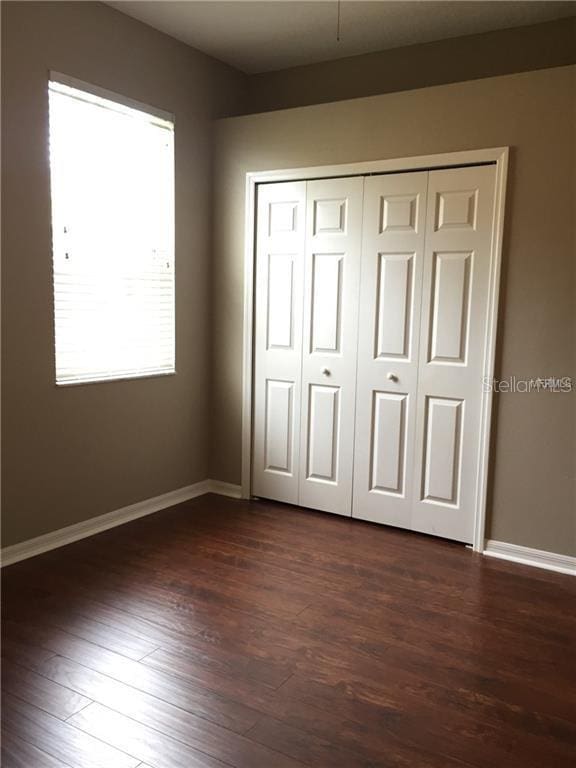 unfurnished bedroom with dark wood-type flooring and a closet