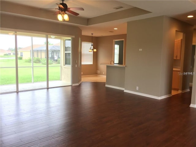 spare room with ceiling fan with notable chandelier, a tray ceiling, dark hardwood / wood-style flooring, and a wealth of natural light