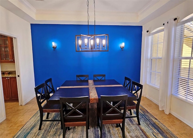 tiled dining area with ornamental molding, a raised ceiling, and a chandelier