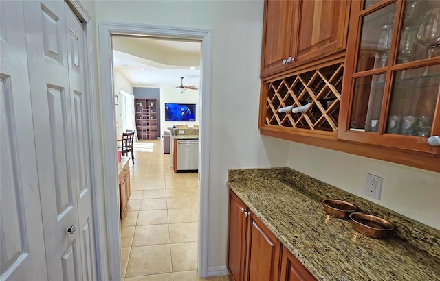 bar featuring stone counters, dishwasher, light tile patterned floors, and ceiling fan