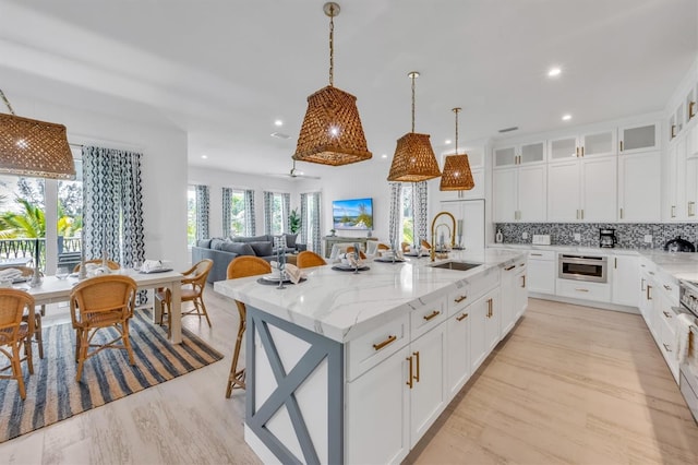 kitchen featuring backsplash, light stone countertops, white cabinetry, and an island with sink