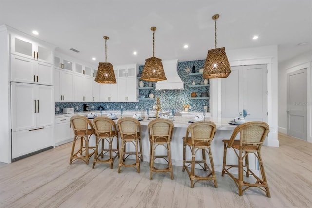 kitchen featuring white cabinets, a kitchen island with sink, hanging light fixtures, and tasteful backsplash