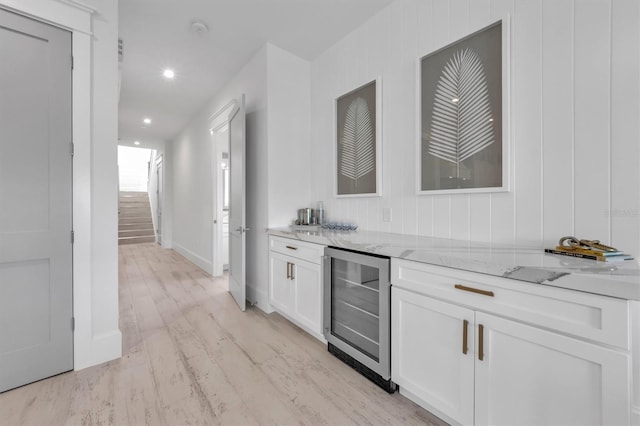 kitchen with white cabinets, light wood-type flooring, light stone countertops, and beverage cooler