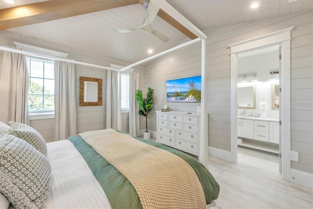 bedroom featuring connected bathroom, light hardwood / wood-style flooring, ceiling fan, and wooden walls