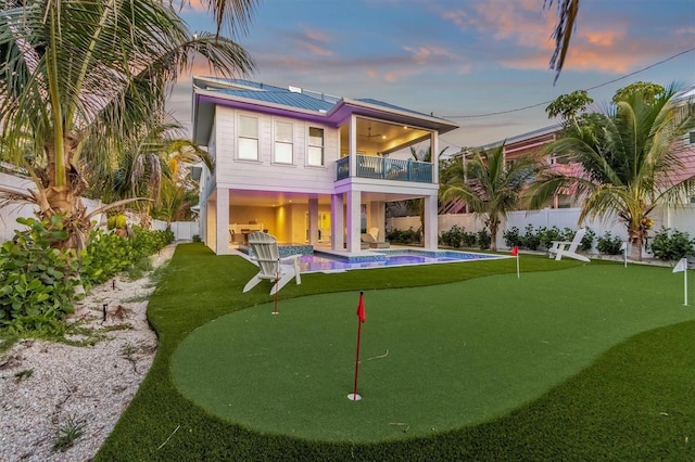 back house at dusk featuring solar panels, a balcony, and a fenced in pool