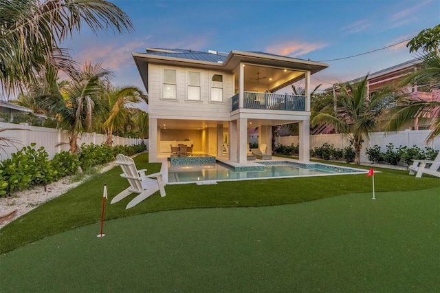 back house at dusk with solar panels, a fenced in pool, ceiling fan, a balcony, and a patio