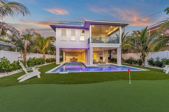 back house at dusk featuring a swimming pool with hot tub, a patio, a balcony, and ceiling fan