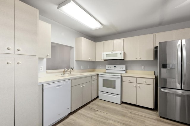 kitchen featuring white appliances, cream cabinetry, sink, and light wood-type flooring