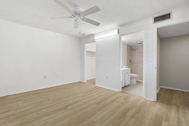 unfurnished bedroom featuring connected bathroom, a walk in closet, light hardwood / wood-style floors, ceiling fan, and a closet