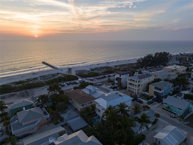 aerial view at dusk featuring a view of the beach and a water view