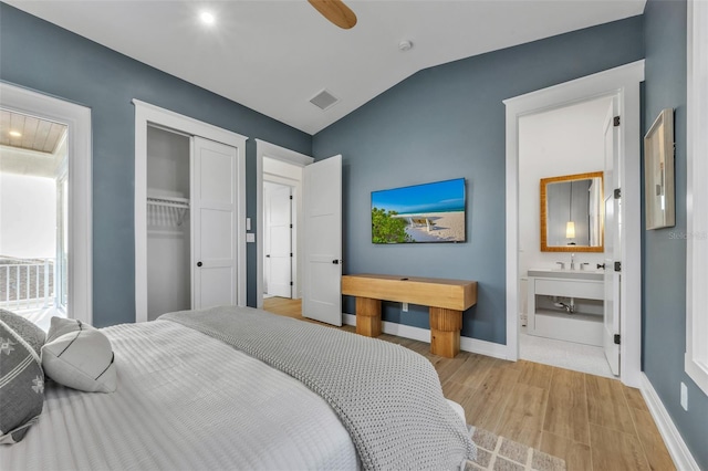 bedroom featuring lofted ceiling, ensuite bathroom, light hardwood / wood-style flooring, ceiling fan, and a closet