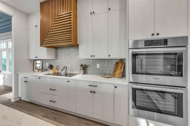 kitchen featuring double oven, light stone counters, white cabinets, and extractor fan