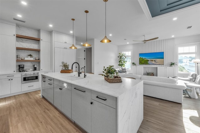 kitchen featuring ceiling fan, sink, hanging light fixtures, a kitchen island with sink, and white cabinets