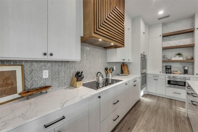 kitchen featuring backsplash, light stone counters, custom range hood, black electric cooktop, and white cabinets