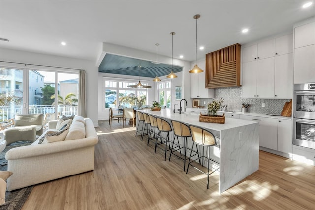 kitchen with pendant lighting, backsplash, white cabinetry, and a kitchen island with sink