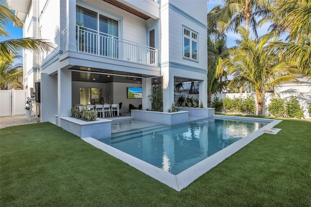 rear view of property featuring a fenced in pool, a balcony, a lawn, and a patio