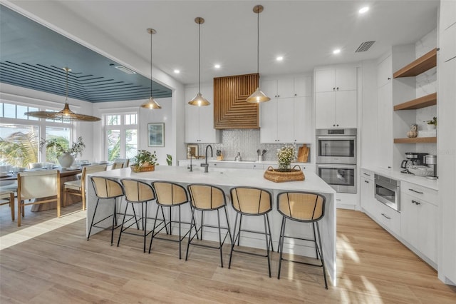 kitchen with stainless steel appliances, a center island with sink, white cabinets, and hanging light fixtures