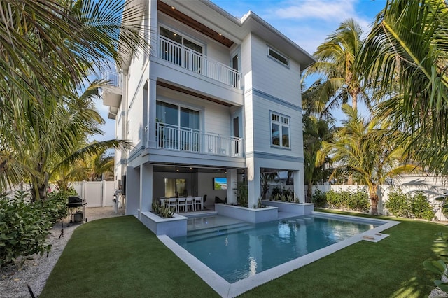 back of property featuring a yard, a balcony, a patio, and a fenced in pool