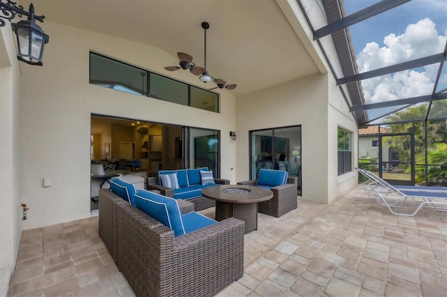 view of patio with a lanai, ceiling fan, and an outdoor living space with a fire pit