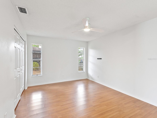 empty room with plenty of natural light, ceiling fan, light wood-type flooring, and a textured ceiling