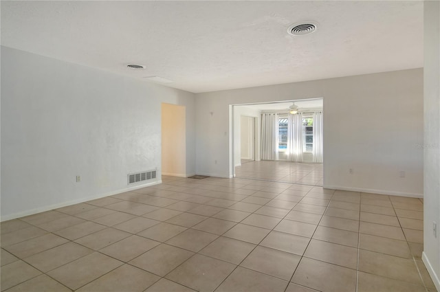 empty room featuring a textured ceiling, light tile patterned flooring, visible vents, and baseboards