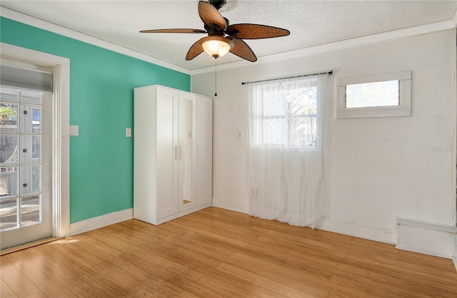 spare room with ornamental molding, light wood-style flooring, baseboards, and a ceiling fan