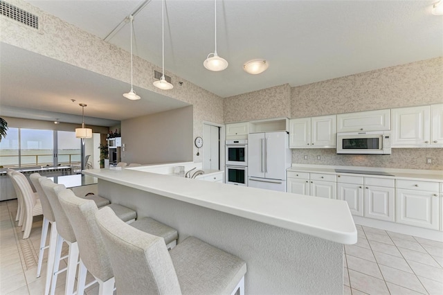 kitchen featuring pendant lighting, white cabinetry, light tile patterned flooring, and white appliances