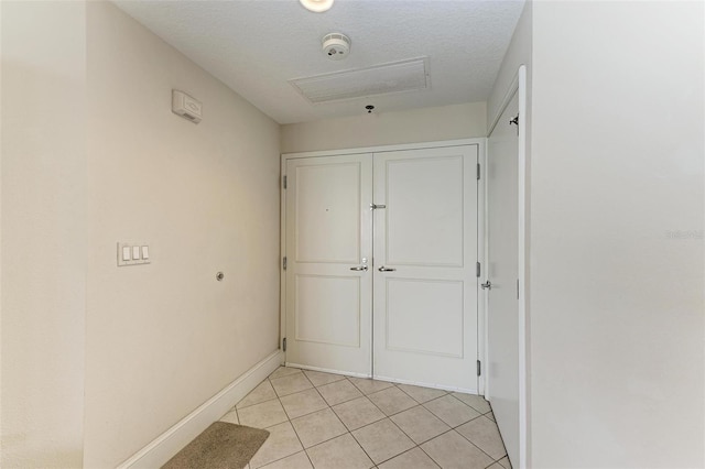 hall with visible vents, a textured ceiling, baseboards, and light tile patterned floors