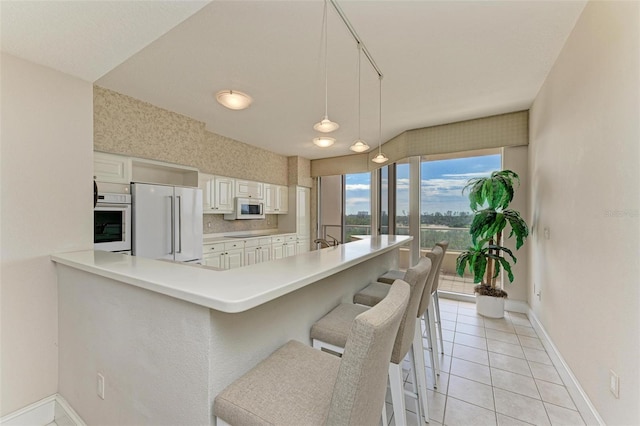 kitchen with white appliances, a breakfast bar, light countertops, white cabinetry, and light tile patterned flooring