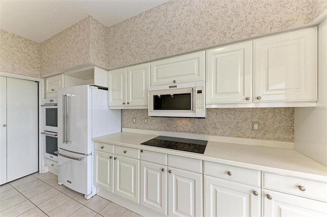 kitchen with light tile patterned floors, light countertops, white cabinetry, white appliances, and wallpapered walls