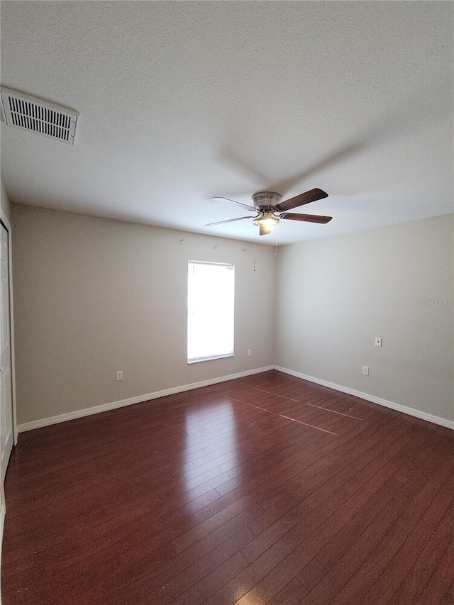 empty room featuring ceiling fan, dark wood-type flooring, and a textured ceiling