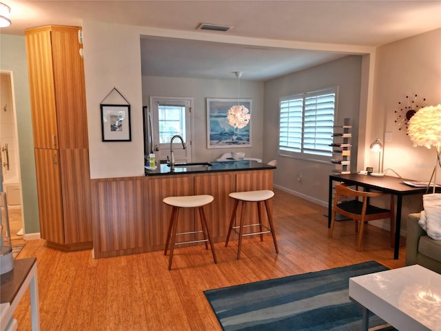 bar with pendant lighting, light wood-type flooring, and sink