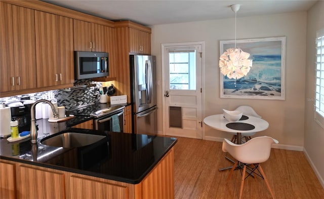 kitchen with tasteful backsplash, hanging light fixtures, appliances with stainless steel finishes, and light hardwood / wood-style flooring