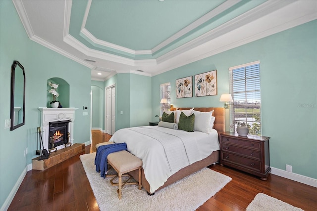 bedroom featuring dark hardwood / wood-style flooring, a raised ceiling, a closet, and ornamental molding