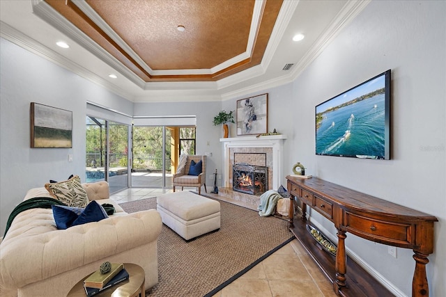 living room with a fireplace, a tray ceiling, ornamental molding, and light tile patterned flooring