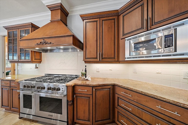 kitchen featuring decorative backsplash, appliances with stainless steel finishes, premium range hood, light stone counters, and ornamental molding