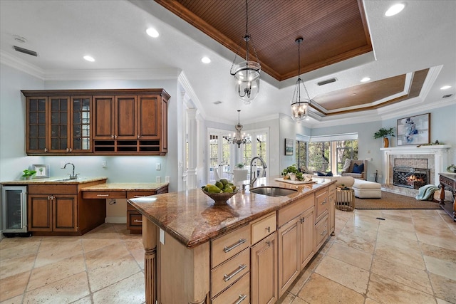 kitchen featuring sink, wine cooler, a tray ceiling, a center island with sink, and ornamental molding