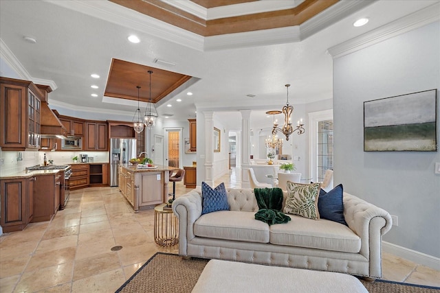 living room featuring a chandelier, a tray ceiling, decorative columns, and ornamental molding