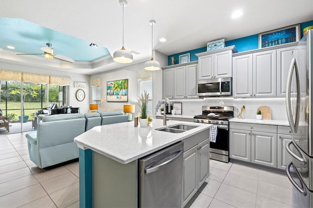 kitchen featuring appliances with stainless steel finishes, gray cabinetry, a raised ceiling, sink, and a center island with sink