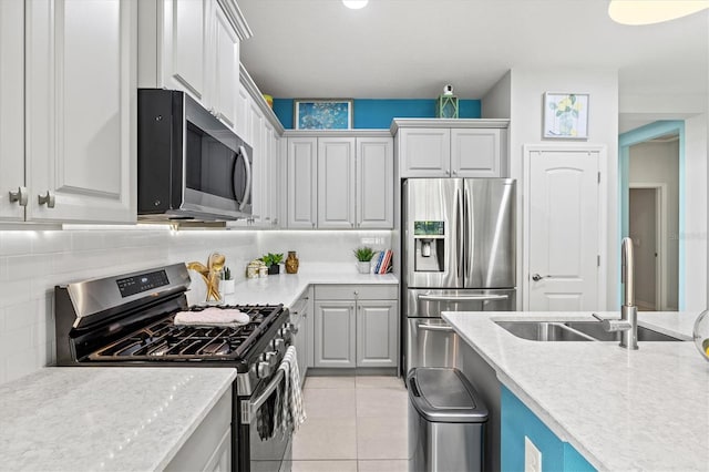 kitchen with decorative backsplash, light stone countertops, stainless steel appliances, sink, and light tile patterned floors