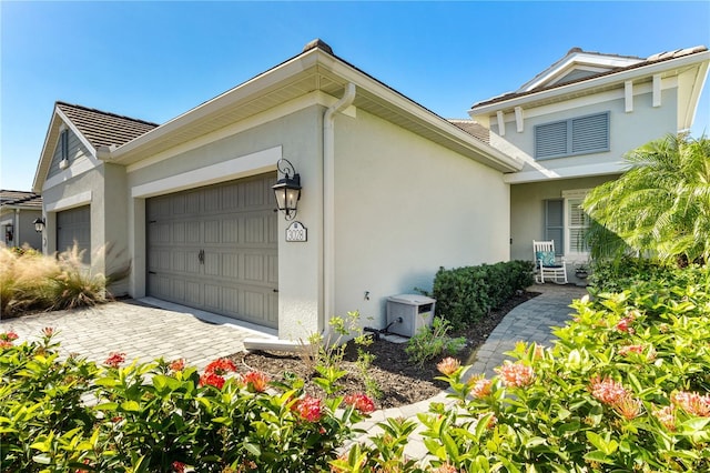 view of side of property featuring a garage, decorative driveway, and stucco siding