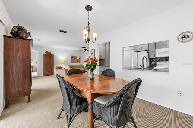 dining area with sink, light colored carpet, and ceiling fan with notable chandelier